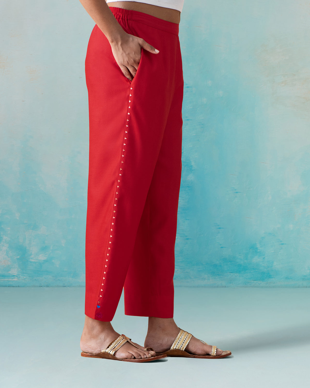 Side view of red Novel pants showing a beaded outer seam and side pocket.