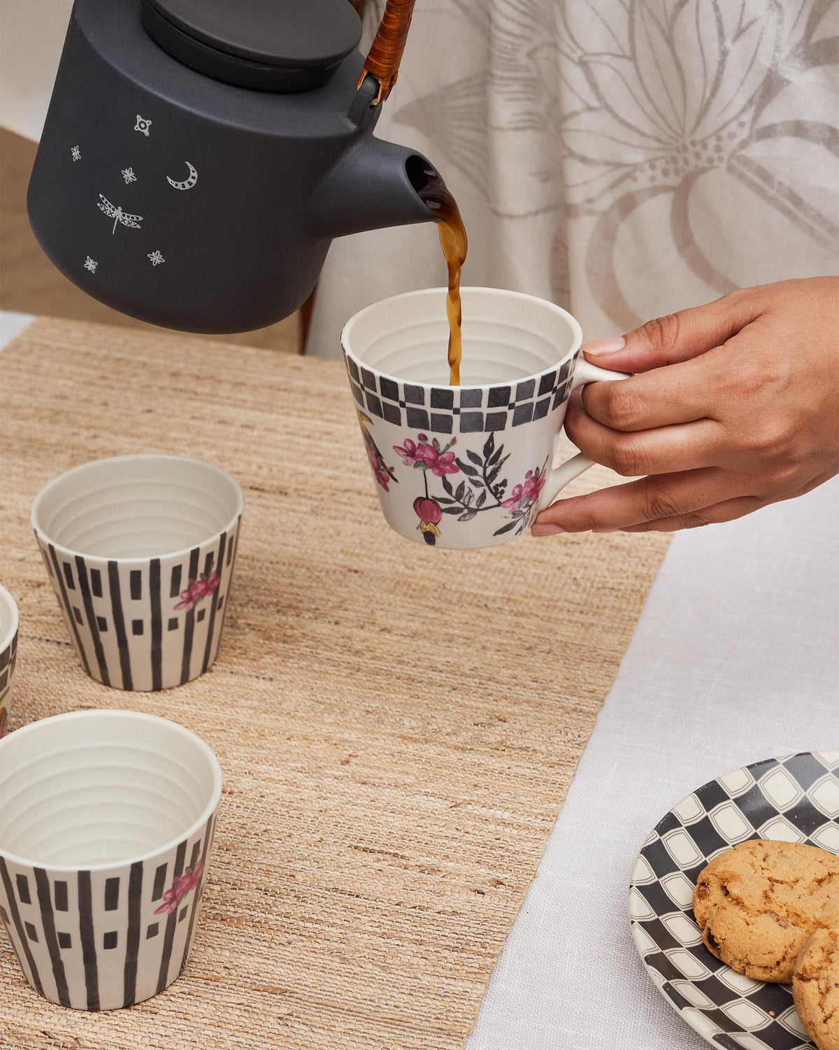 Nectar espresso mug with pink flowers being filled, with matching striped cups nearby.