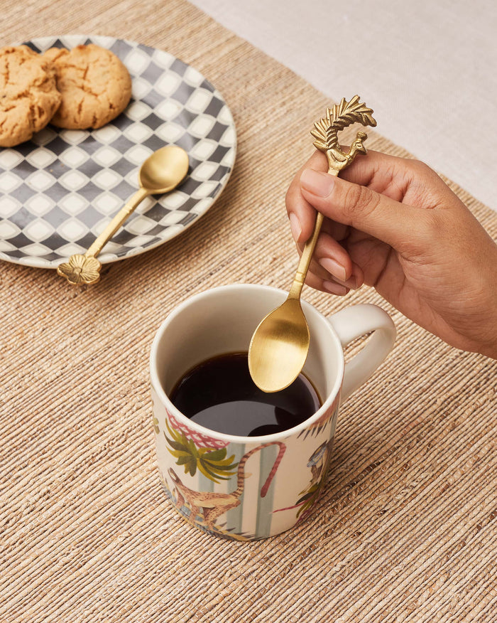 Hand holding a brass Mizo coffee spoon with a peacock finial over coffee.