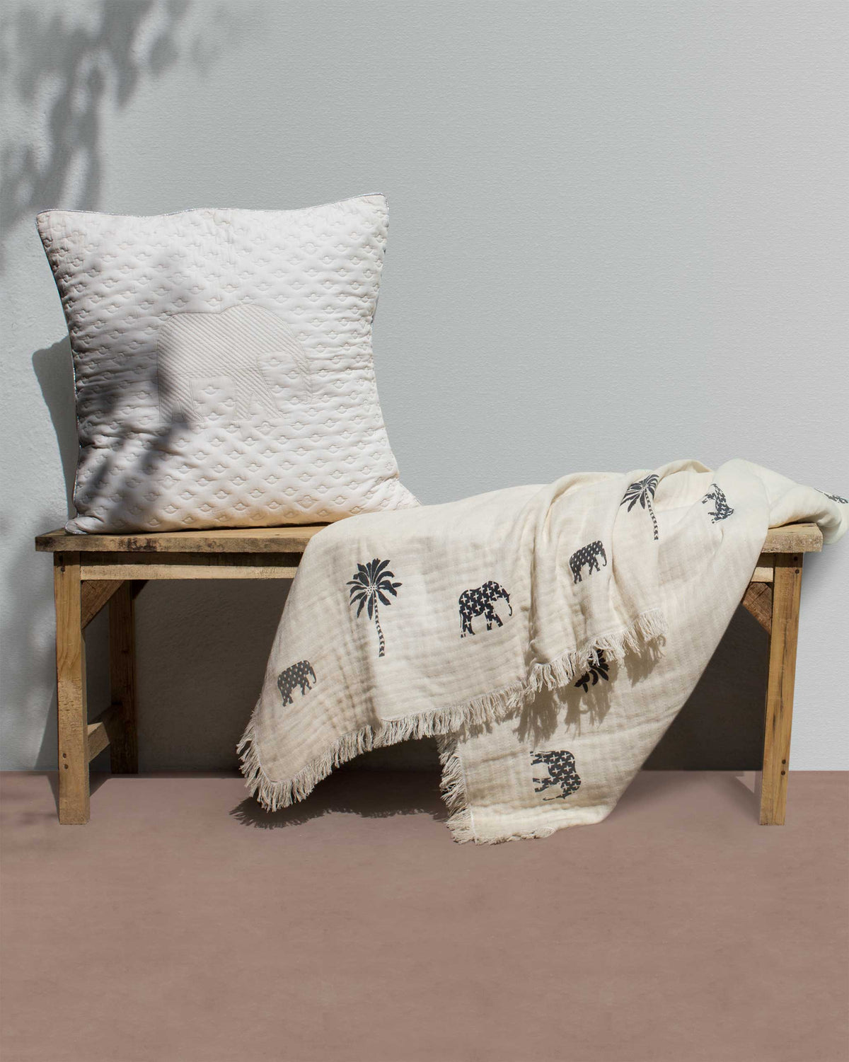Colombo throw with elephant and palm print draped on a wooden bench.