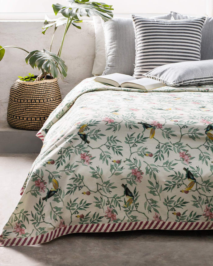 Ivory Nakano bed cover with toucans, foliage, and a maroon diagonal striped border.