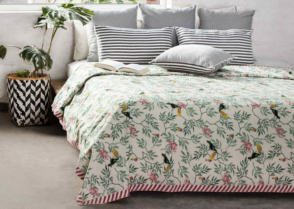Nakano bed cover draping a bed corner, showing toucans and a striped border.