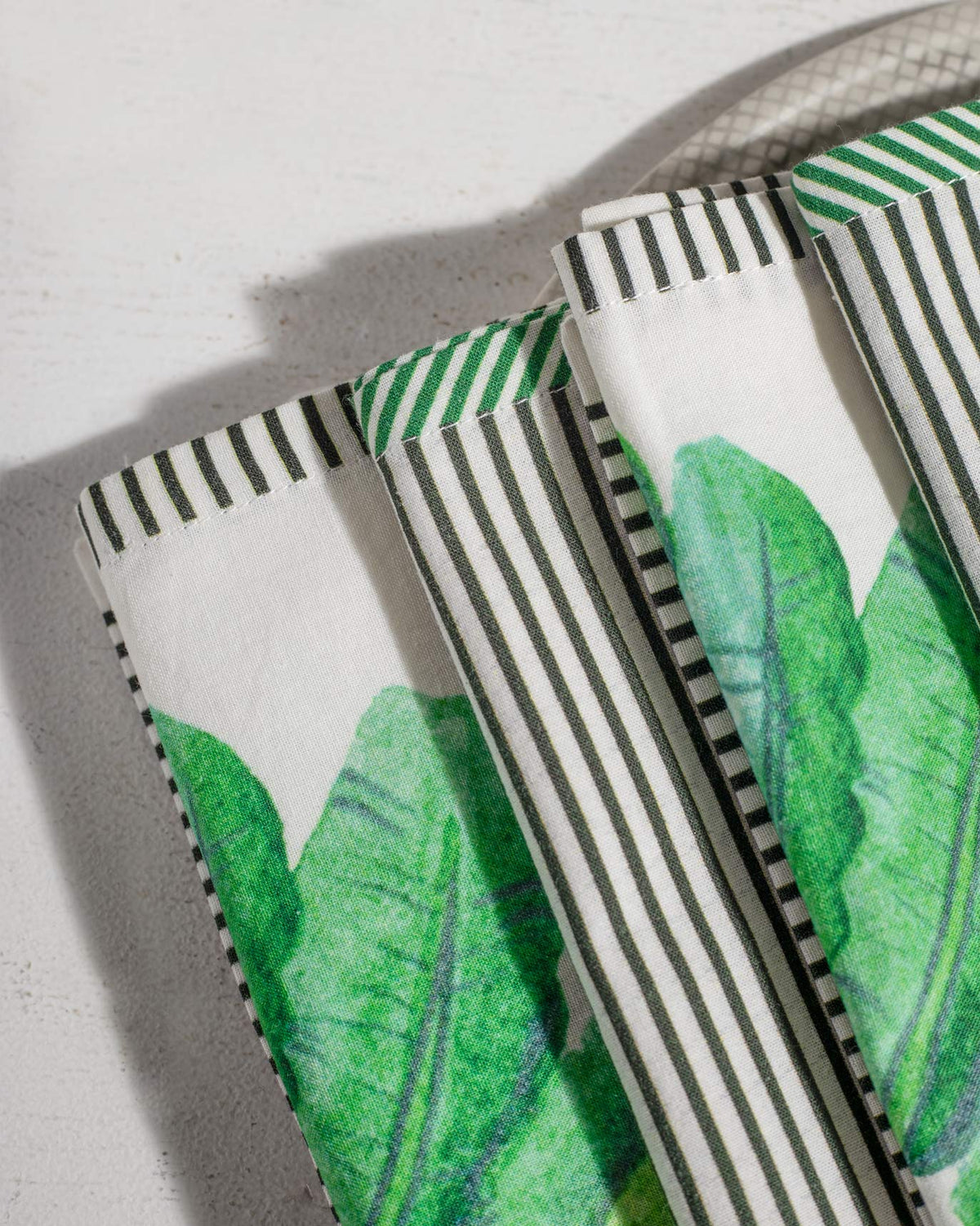 Close-up of Ravenala napkins showing green leaf print and striped hems.