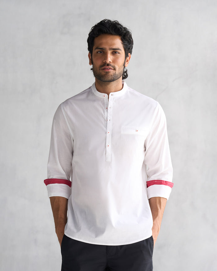 Person wearing a white Pondicherry shirt with red cuff trim.