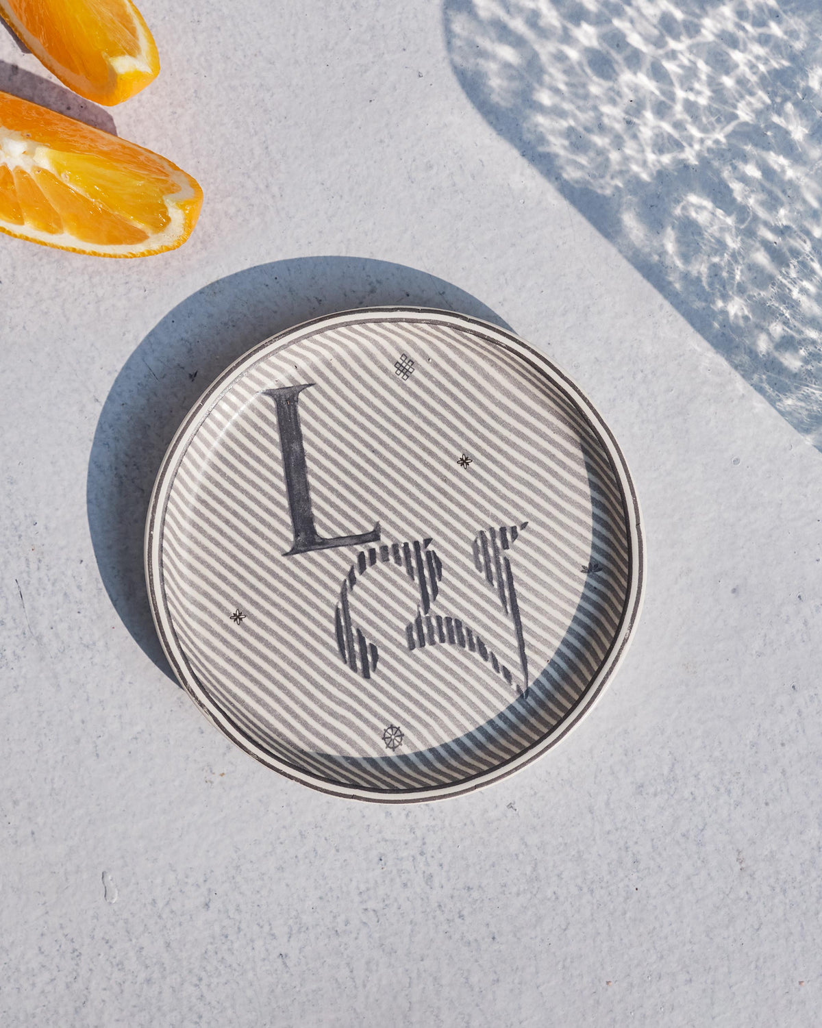 Akshar Coaster with a letter L on grey diagonal stripes.