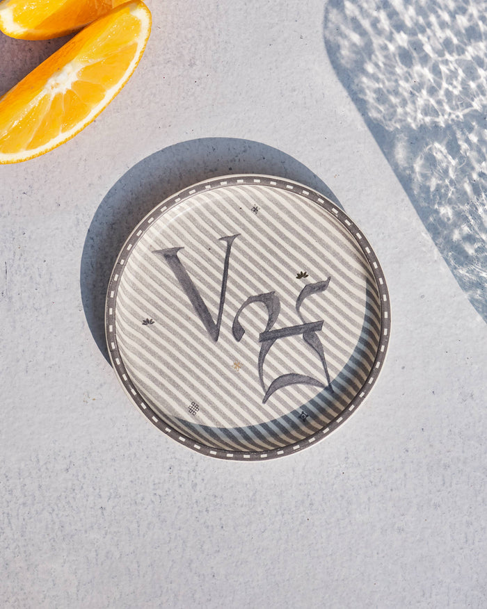 Akshar Coaster - V laid flat, showing the grey V glyph on diagonal stripes.