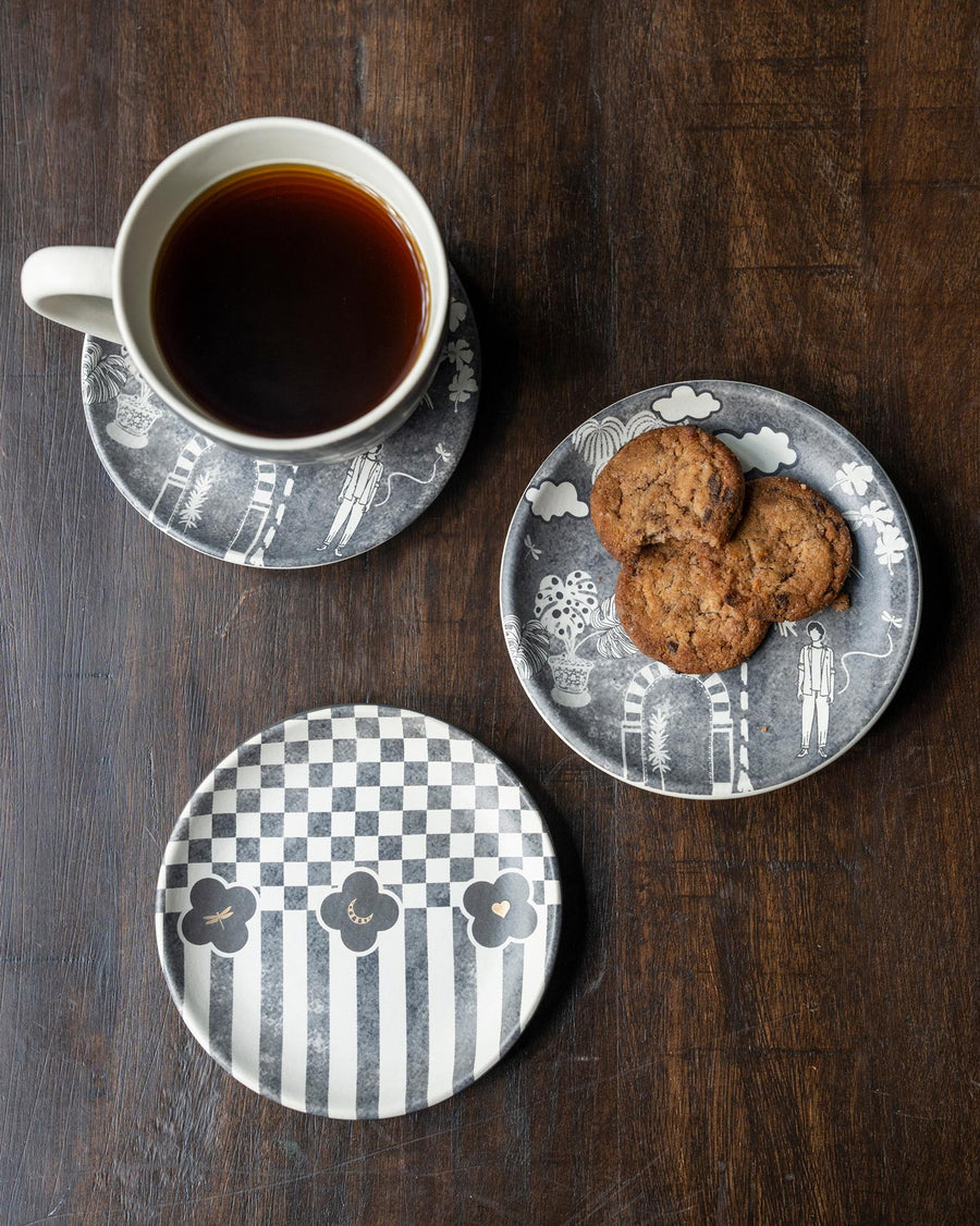 Mandovi plates with cookies beside a cup of black coffee on dark wood
