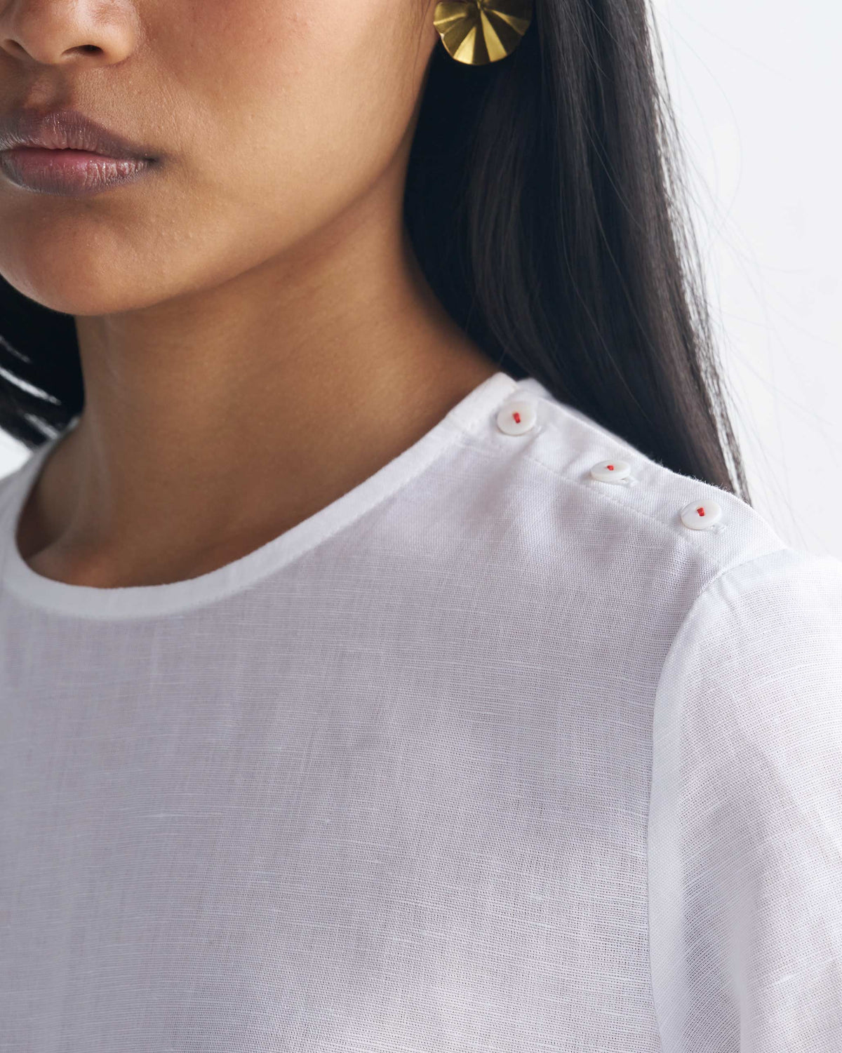 Close-up of a white High Slit Top showing shoulder buttons with red stitching.