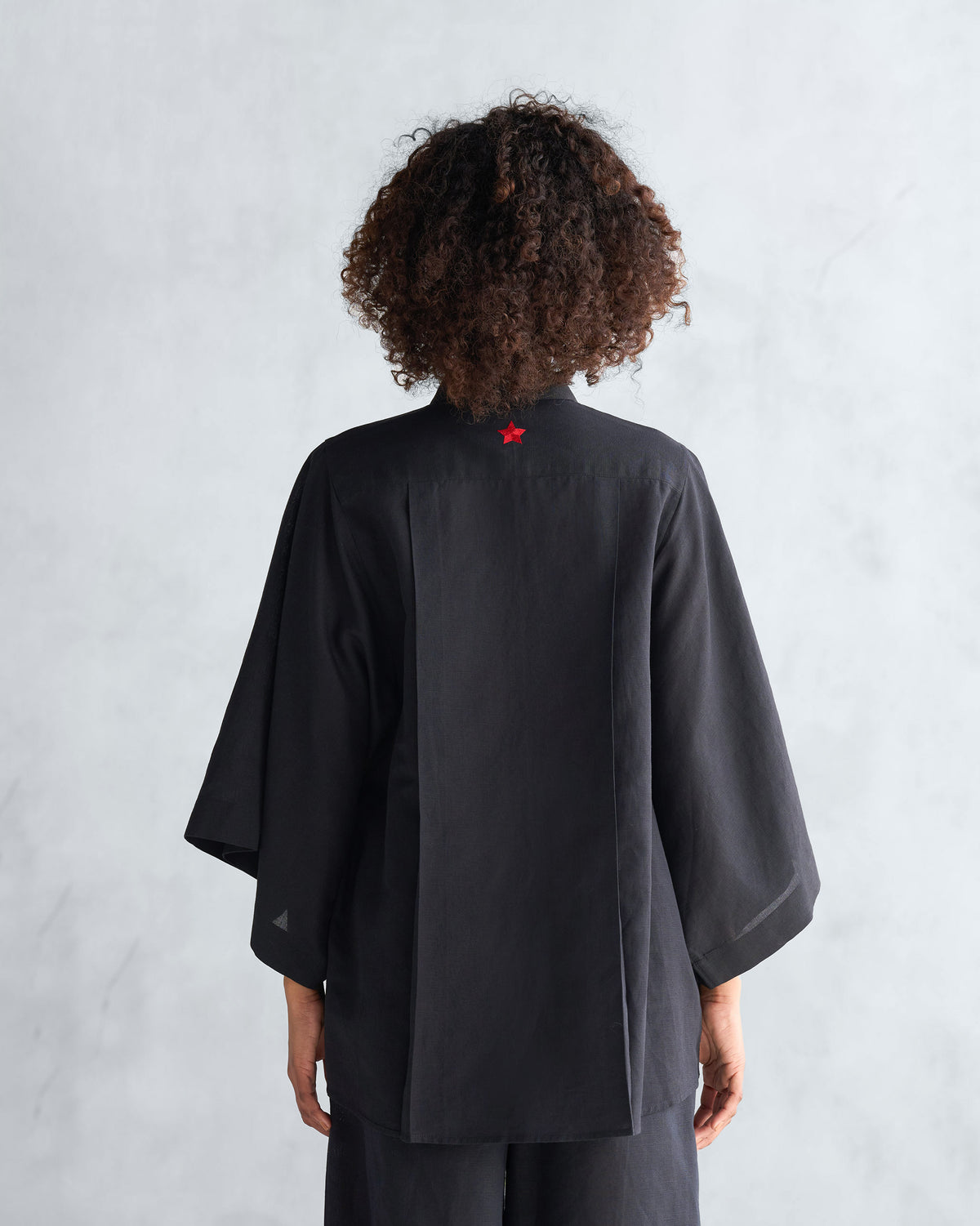 Back of a black Drop armhole shirt with a red embroidered star at the collar.