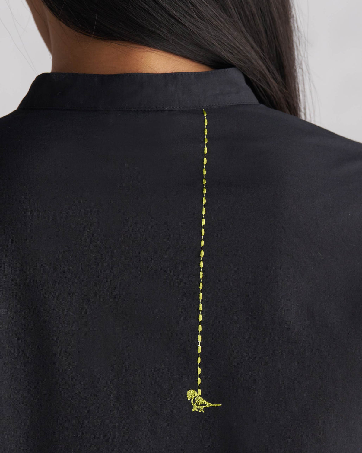 Close-up of lime green bird embroidery on the back of a black long kurta.