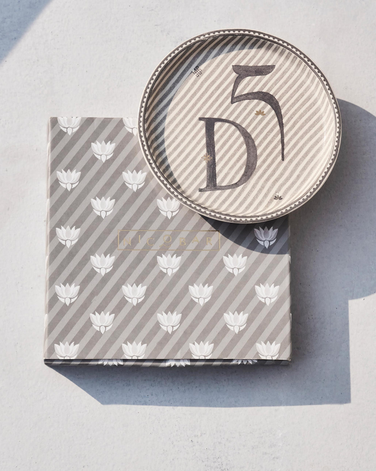 Akshar Coaster with a letter D set on its lotus-print gift box.