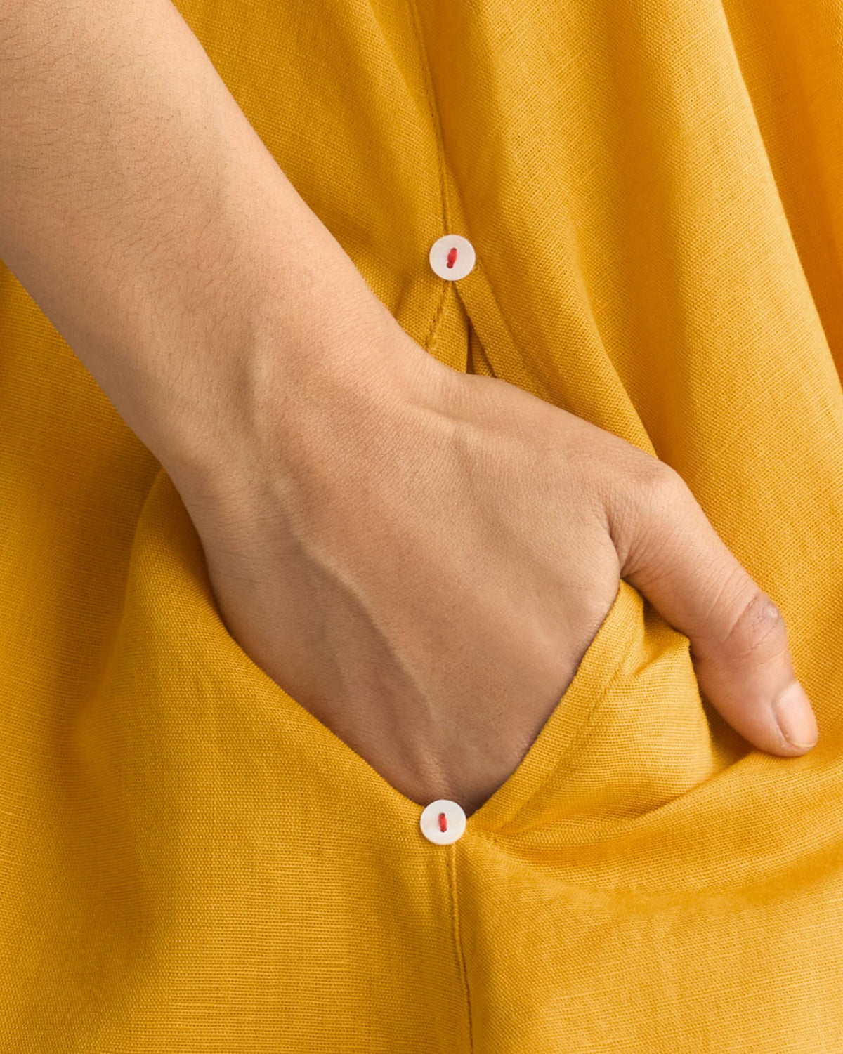 Close-up of a mustard yellow Double layer dress pocket with small buttons.