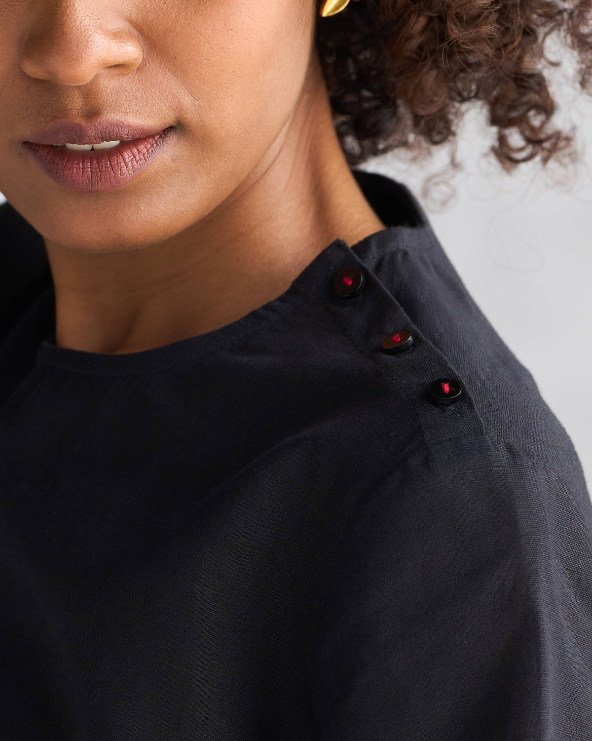 Close-up of a black High Slit Top showing shoulder buttons with red stitching.