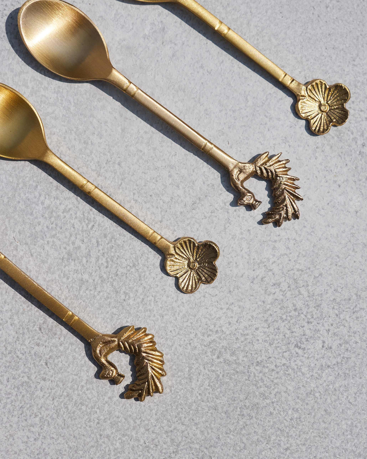 Close-up of peacock and flower finials on brass Mizo coffee spoons.