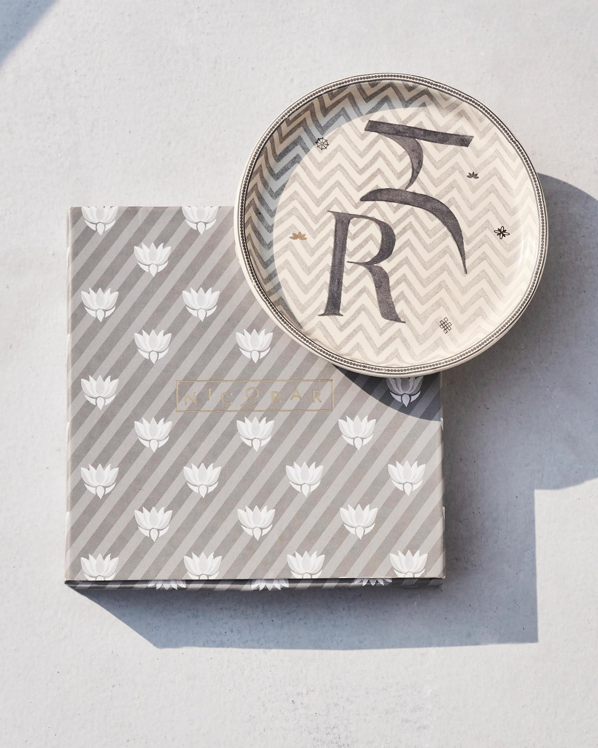 Akshar Coaster - R resting on its grey lotus-print box.