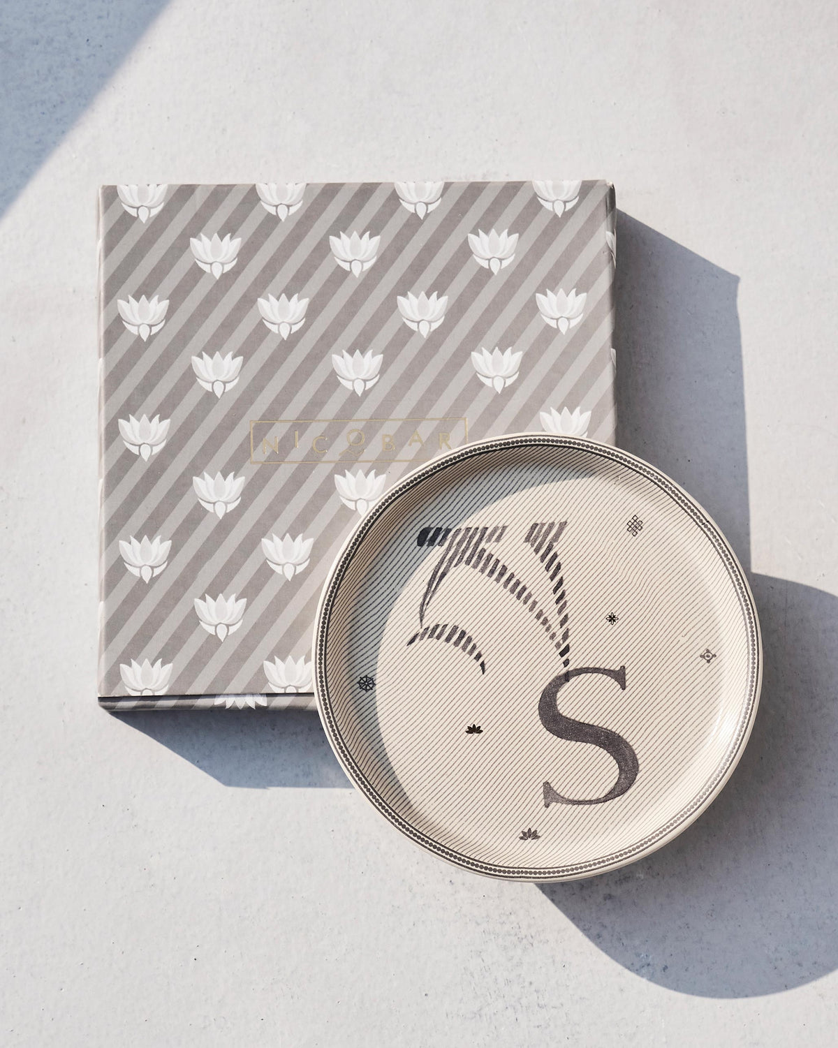 Akshar coaster S beside its grey striped Nicobar gift box with lotus motifs.