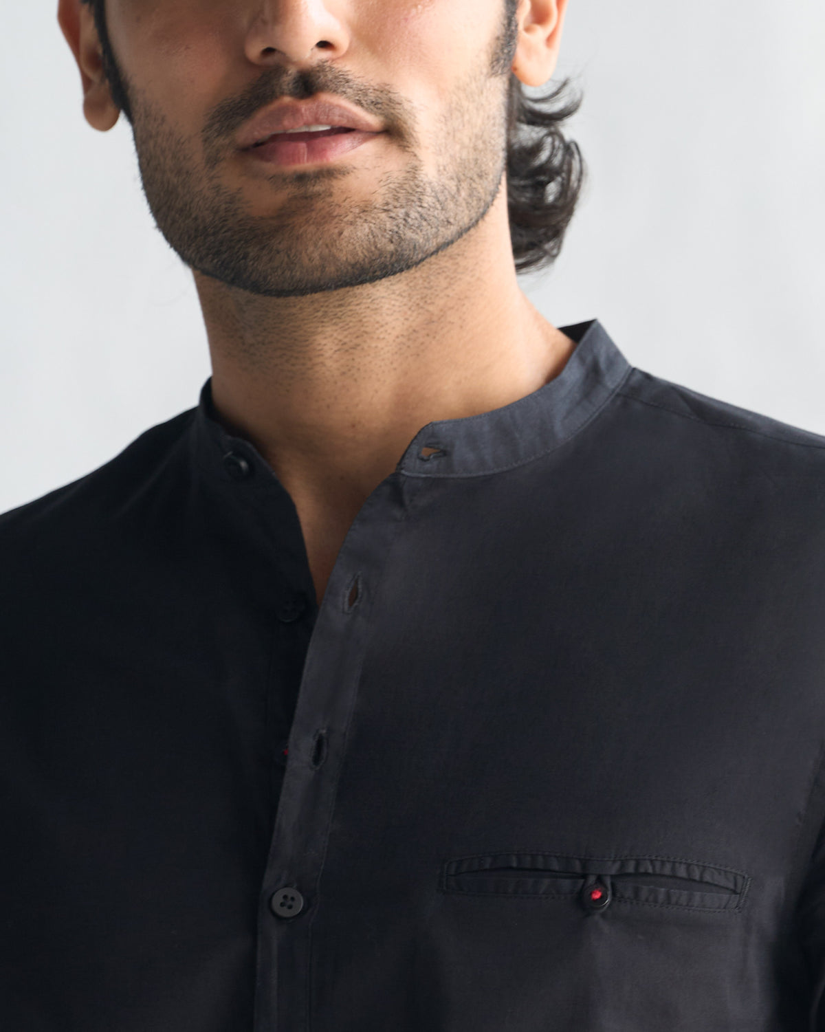 Close-up of a black Pondicherry shirt showing a chest pocket with a red detail.