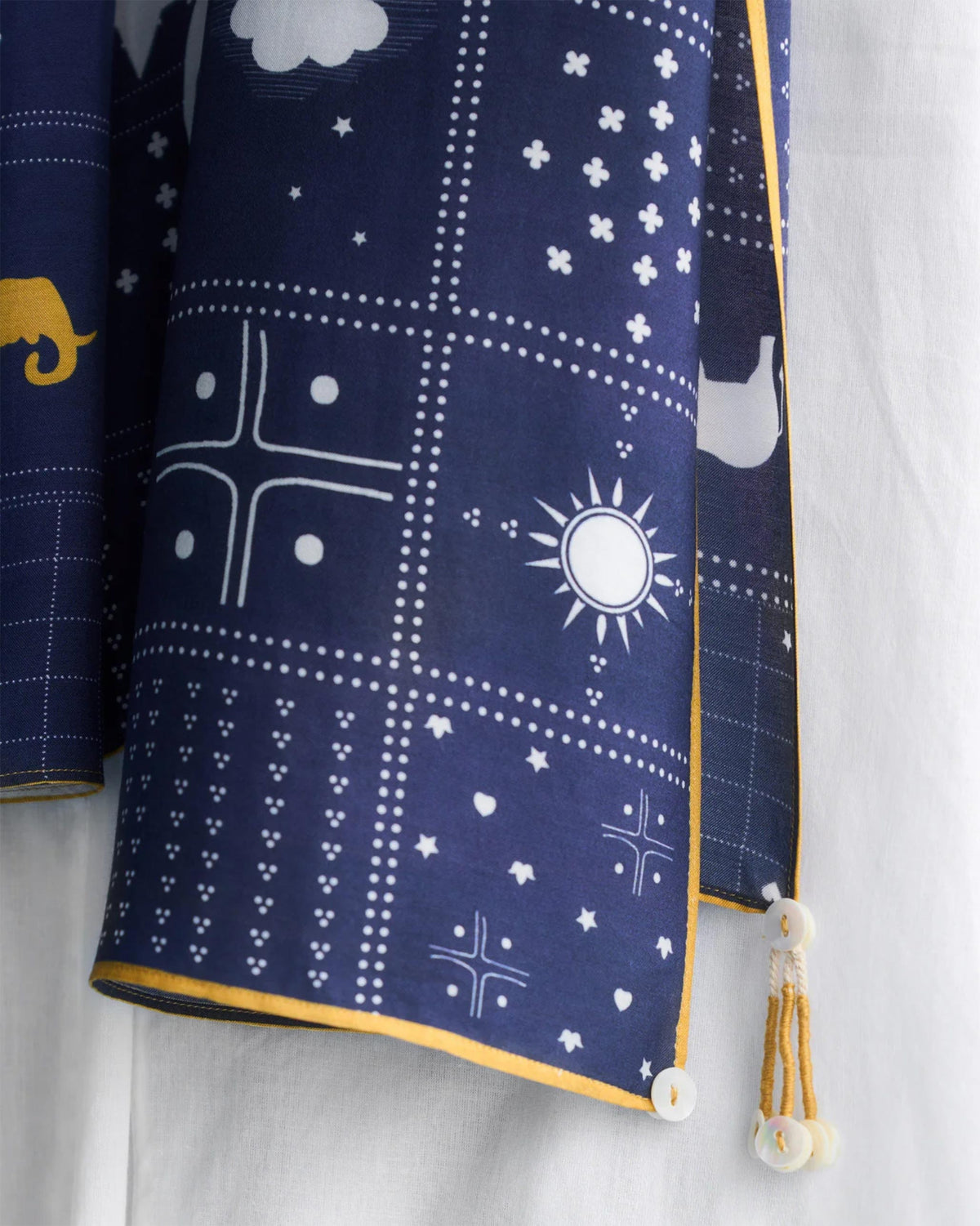 Close-up of navy Parken scarf showing white sun and star motifs with a yellow edge.