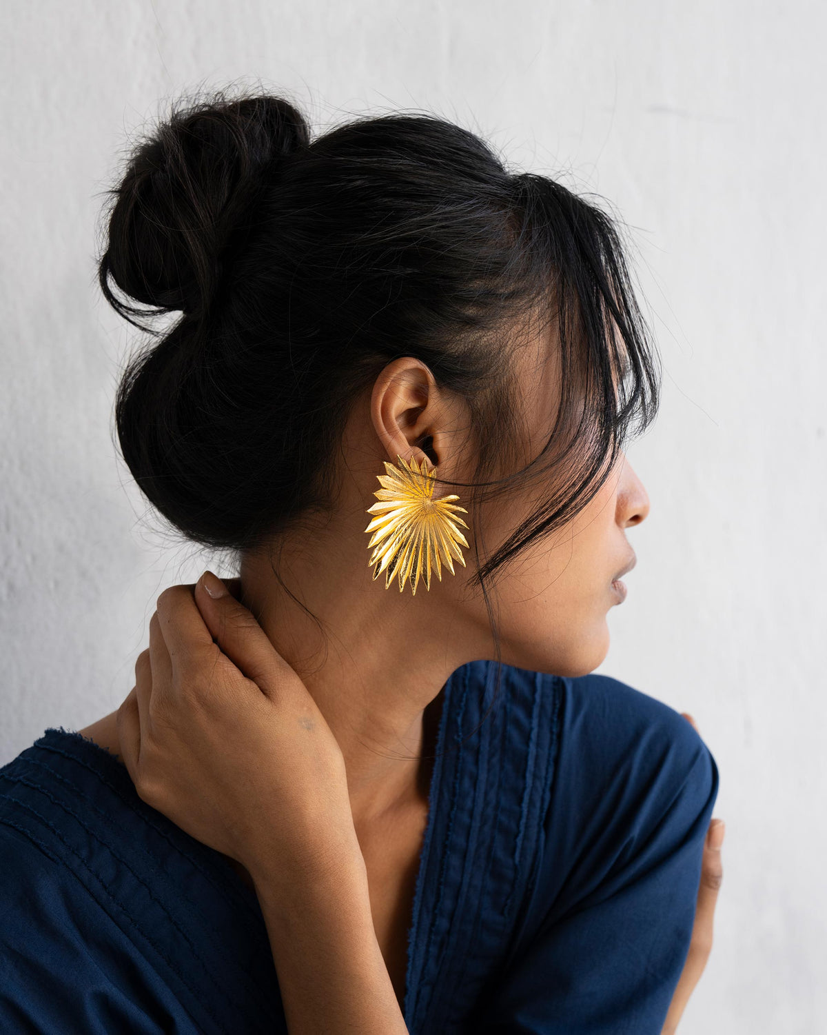 Gold palm leaf earring worn in profile against the jaw.