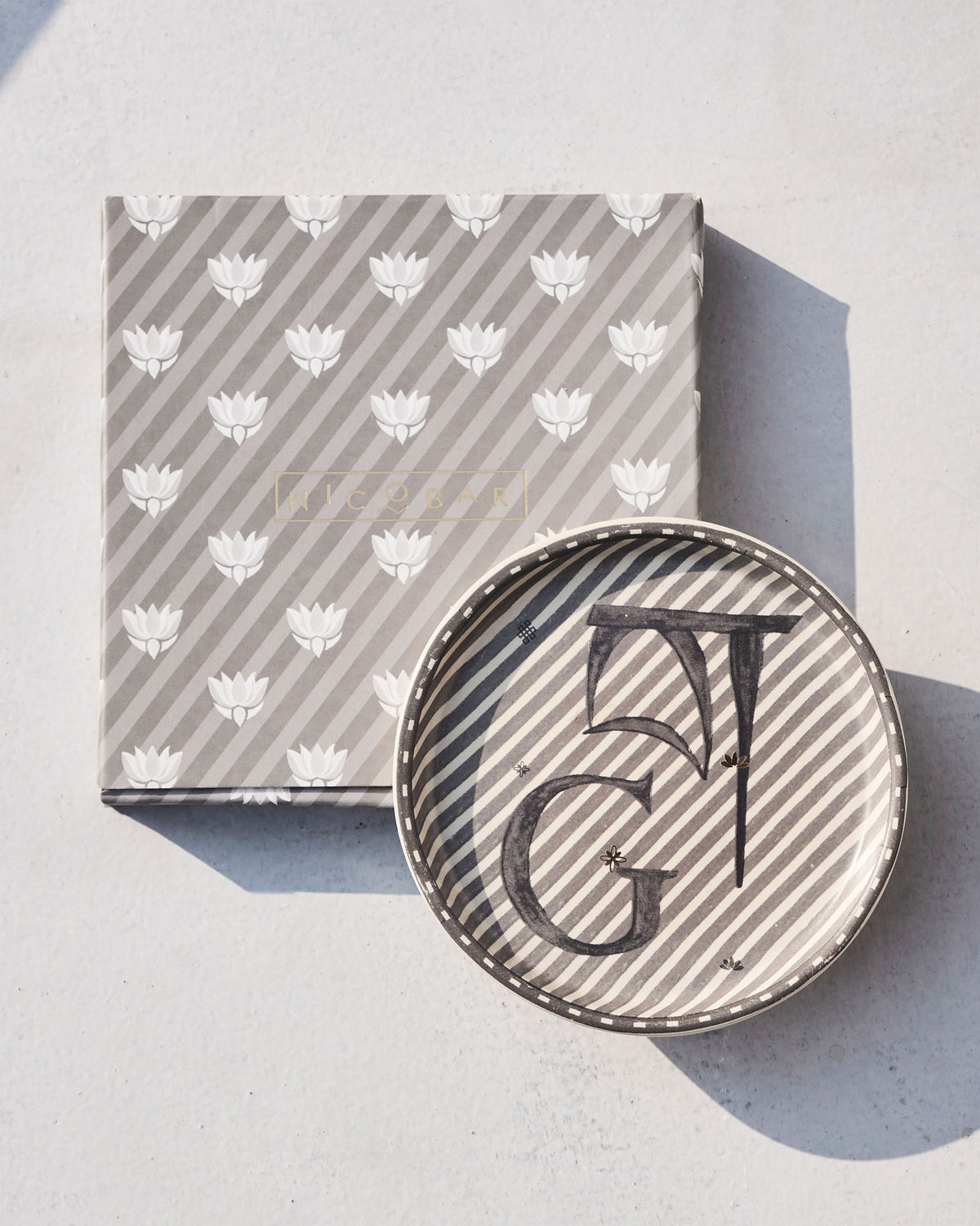 Akshar Coaster with a letter G resting on its lotus-print gift box.