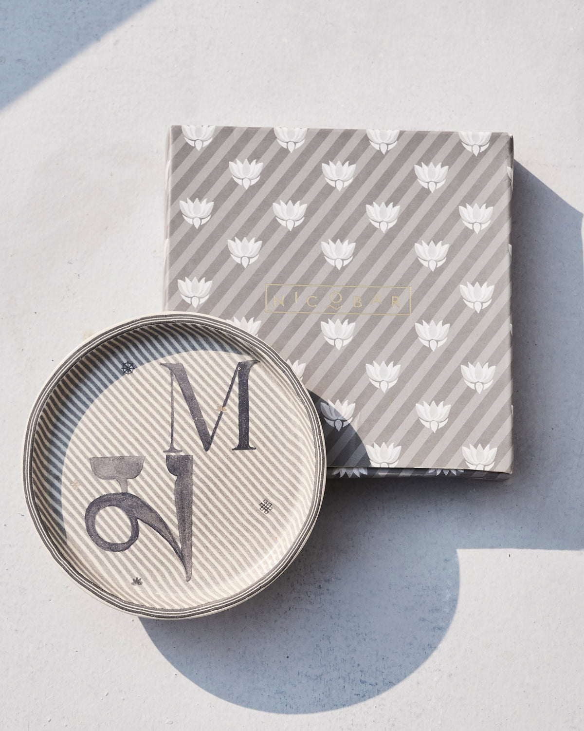 Akshar coaster M on its grey striped Nicobar gift box with lotus motifs.