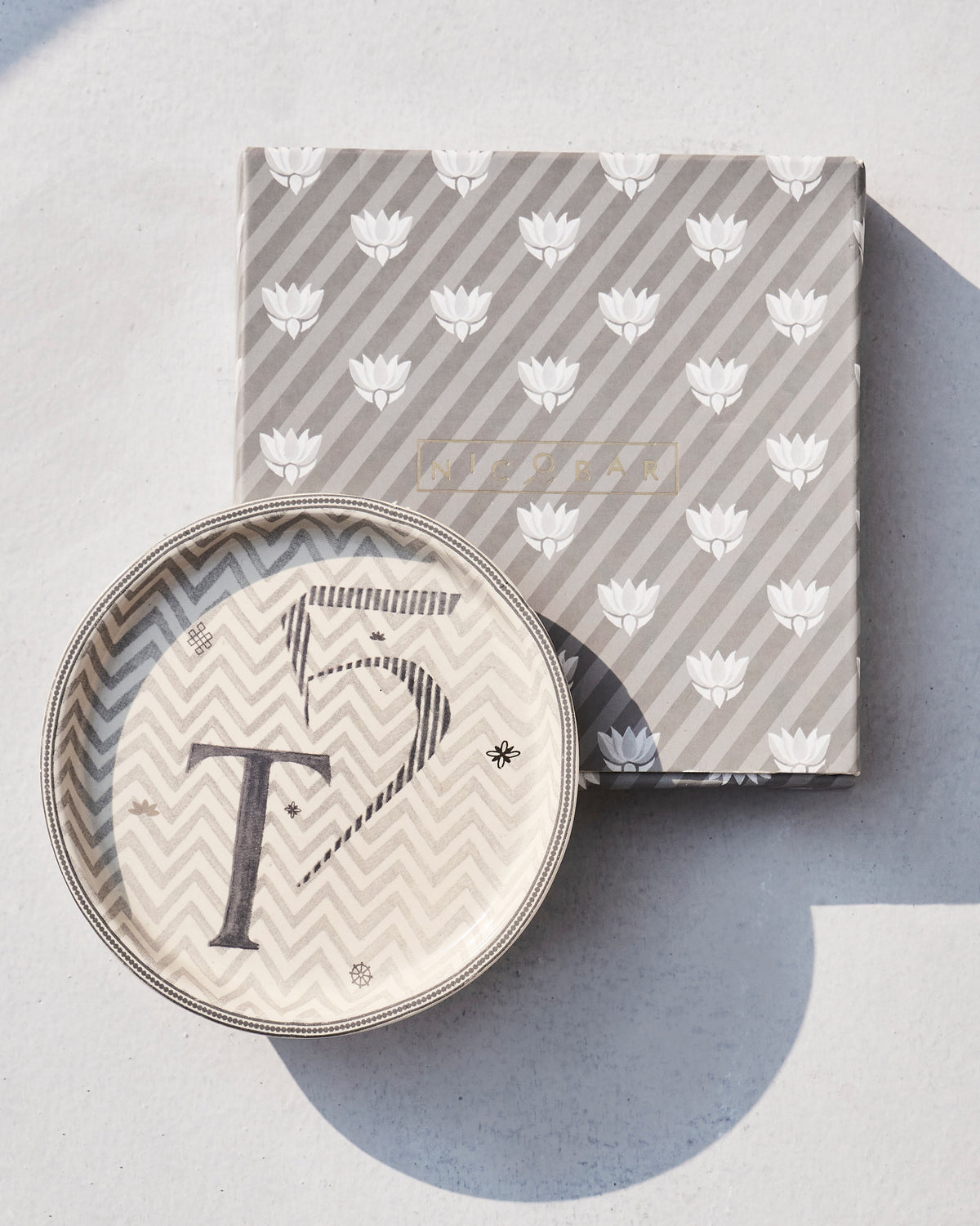 Akshar Coaster - T resting on its grey lotus-print box.