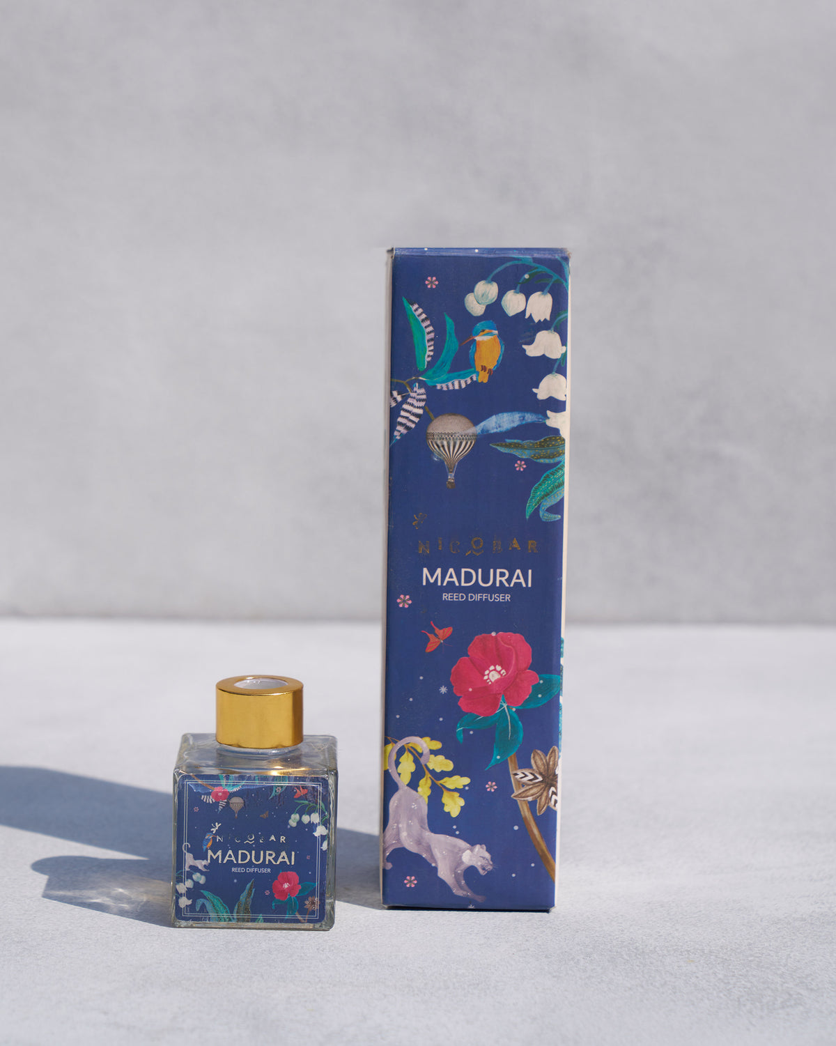 Madurai Reed Diffuser bottle beside its blue box with birds and flowers.