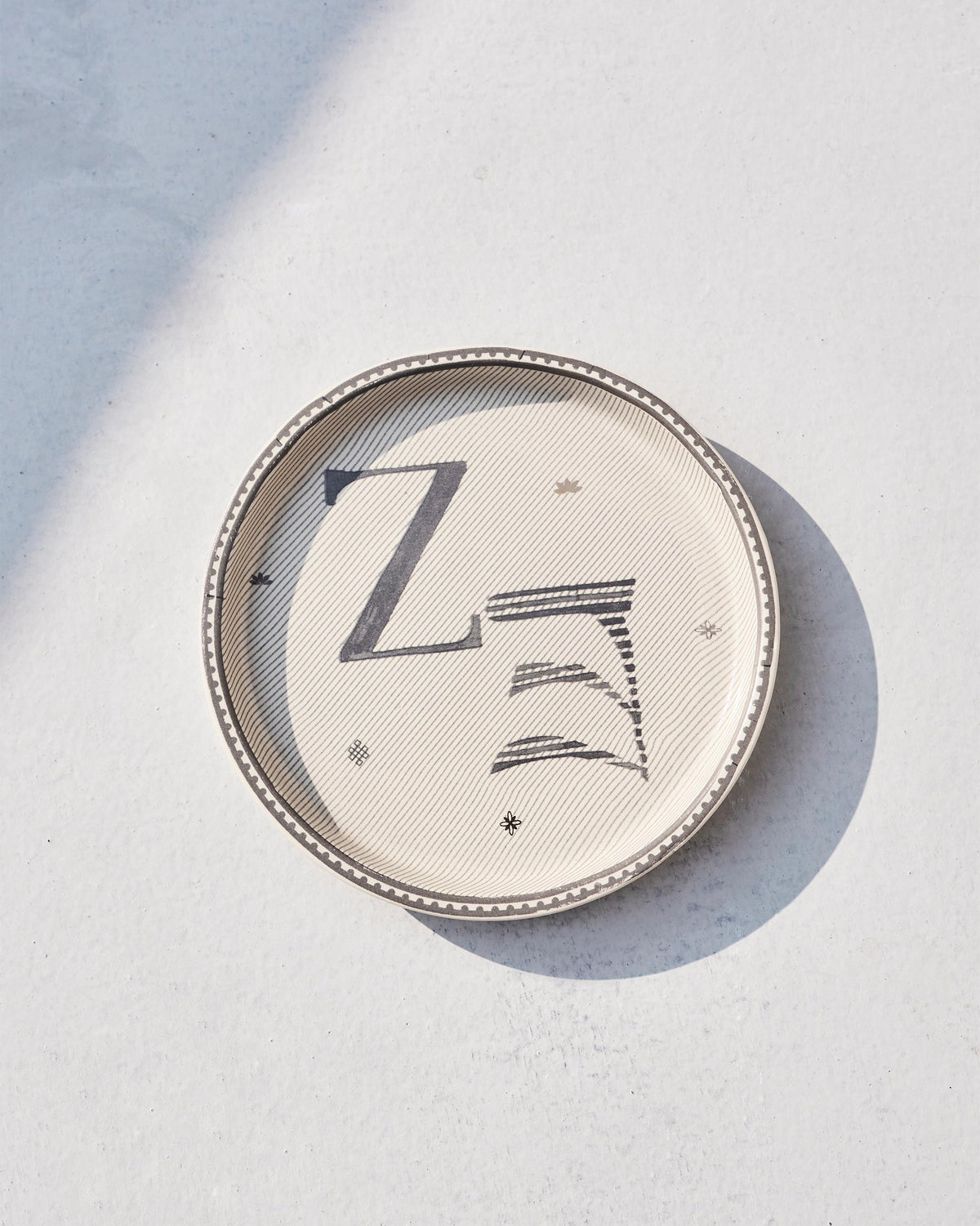 Akshar Coaster - Z lying flat with its beaded rim and grey Z glyph.