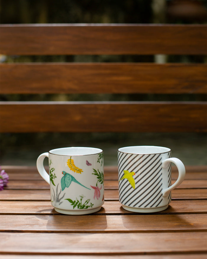 Pair of Tota Mugs, one with a green bird and botanical print, one with stripes and a yellow bird.