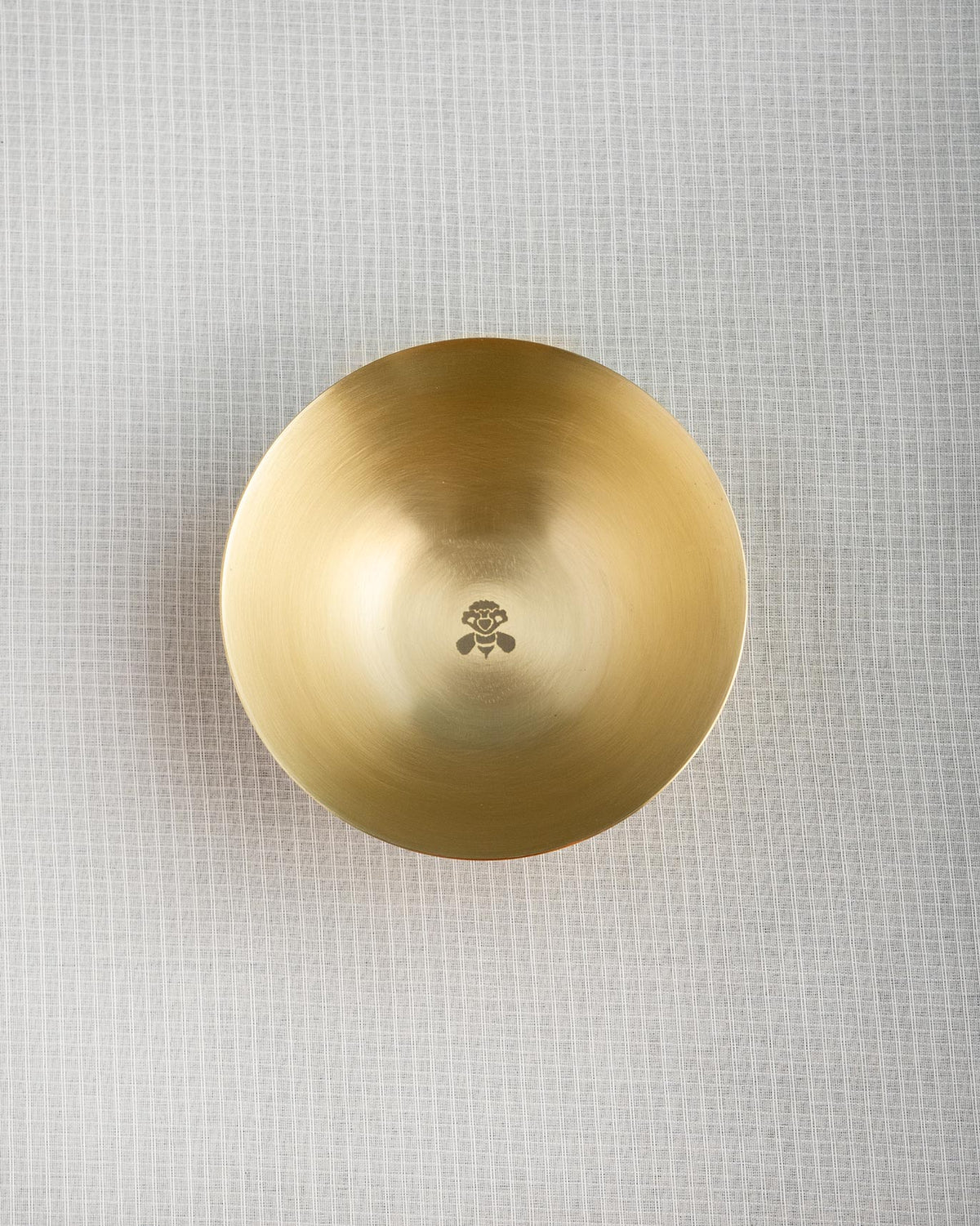 Overhead view of a brass Madhu katori with a bee motif in the centre.
