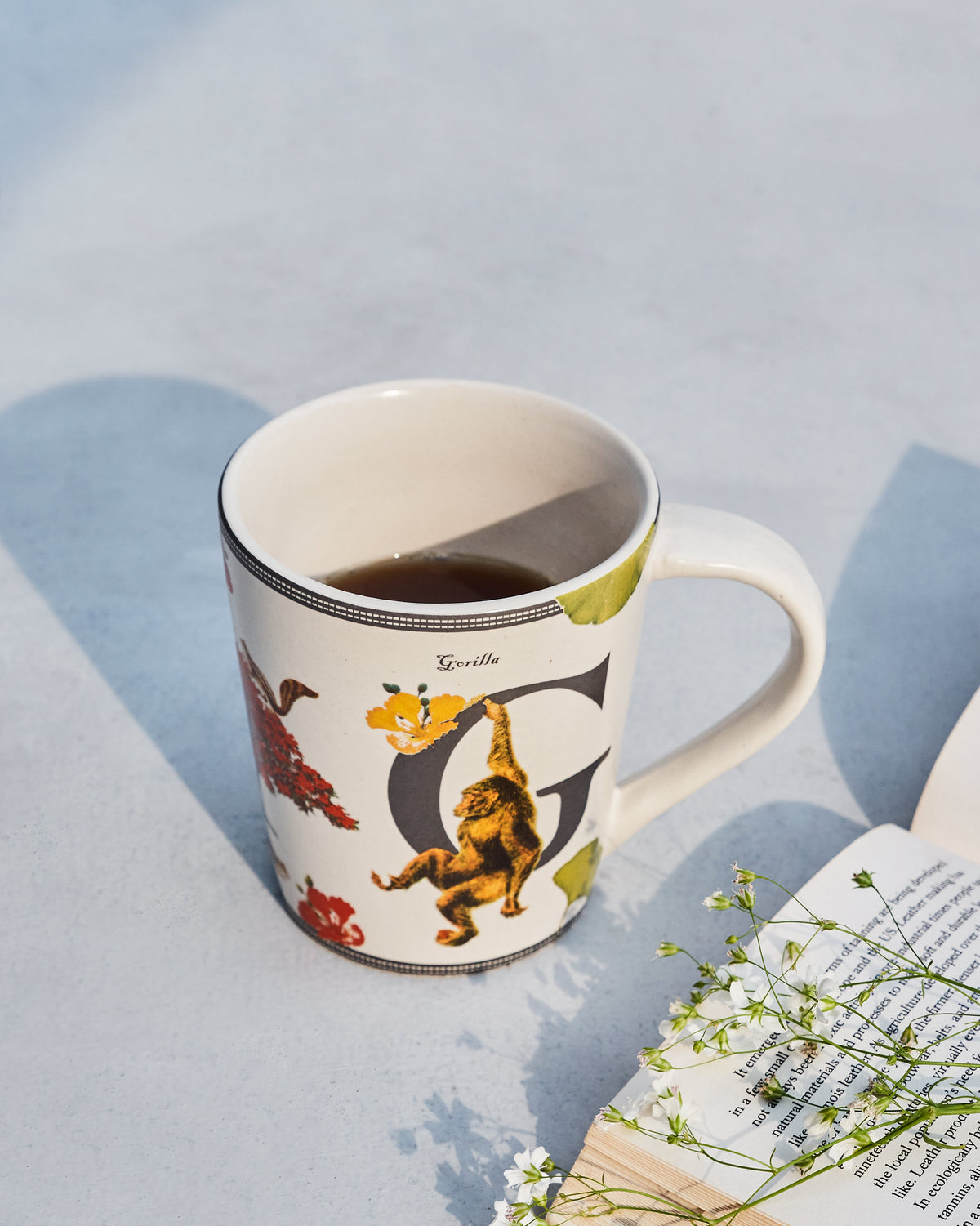 The Gulmohar Mug filled with a dark drink beside an open book.