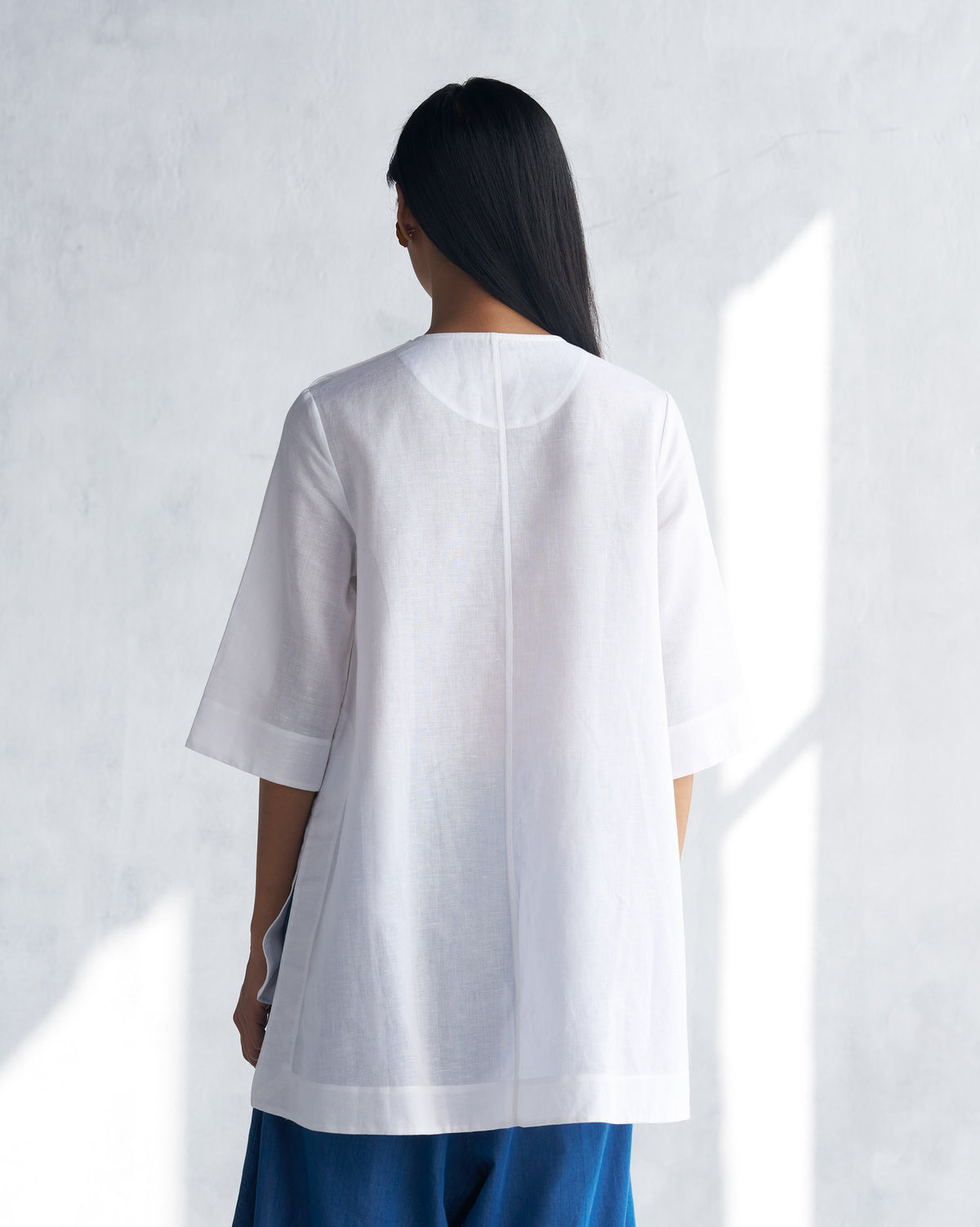Back of a white High Slit Top with a center seam and side slits.