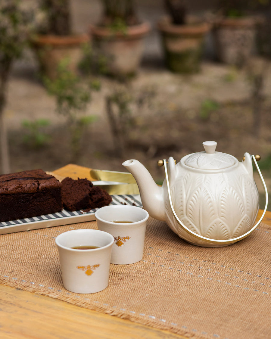 The white Teesta teapot and two cups beside chocolate cake outdoors