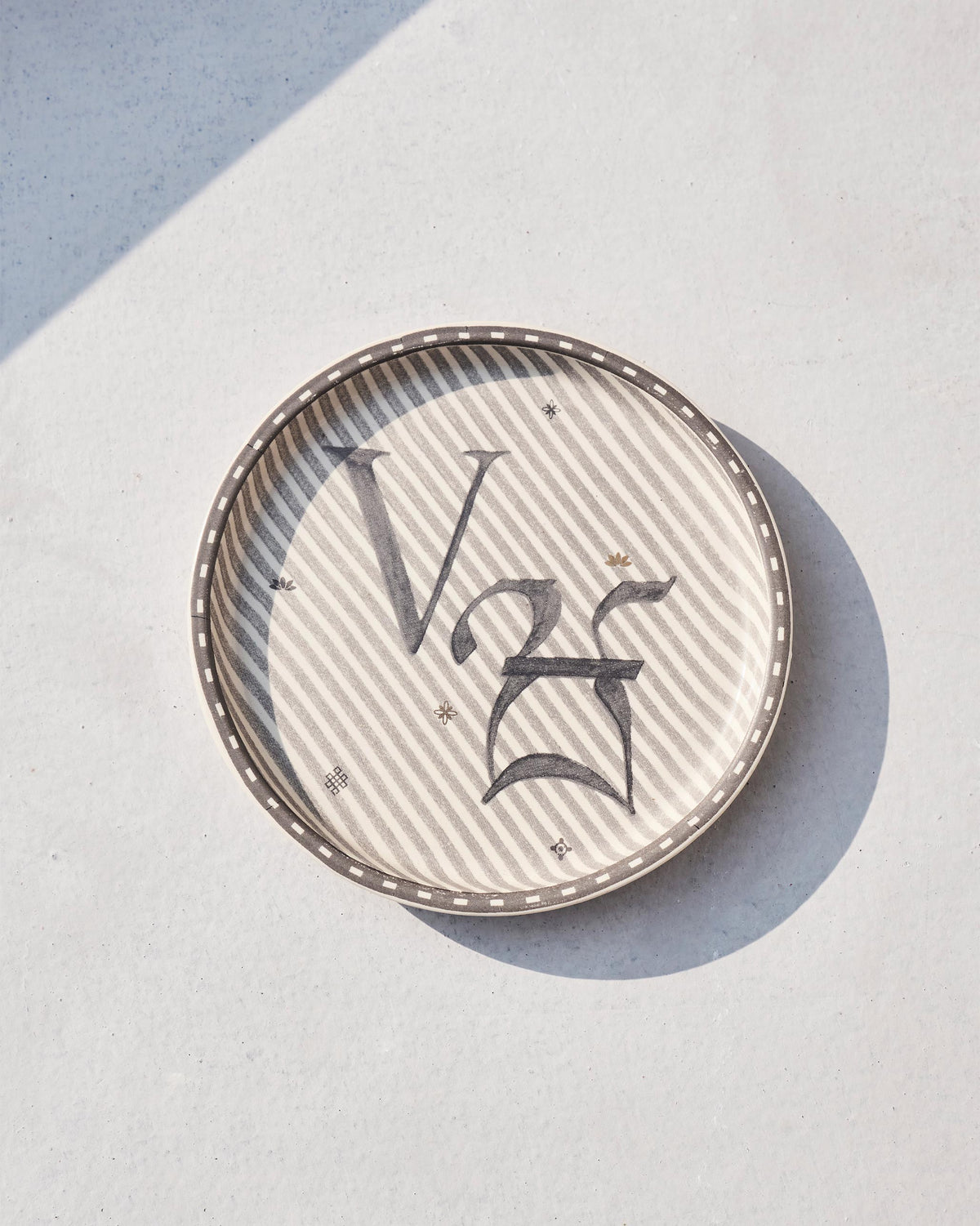 Akshar Coaster - V lying flat, showing its beaded rim and grey V glyph.