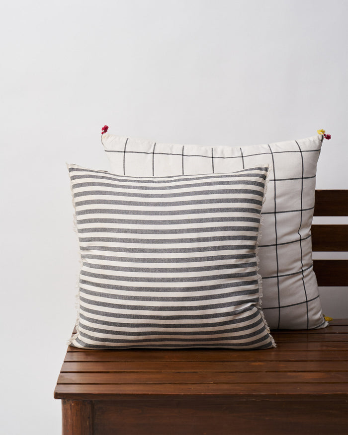 Black & White cushion cover in cream with black stripes, on a wooden bench.