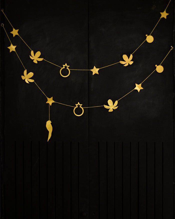 Kachnaar Toran with gold star, flower and ring motifs hanging against black.