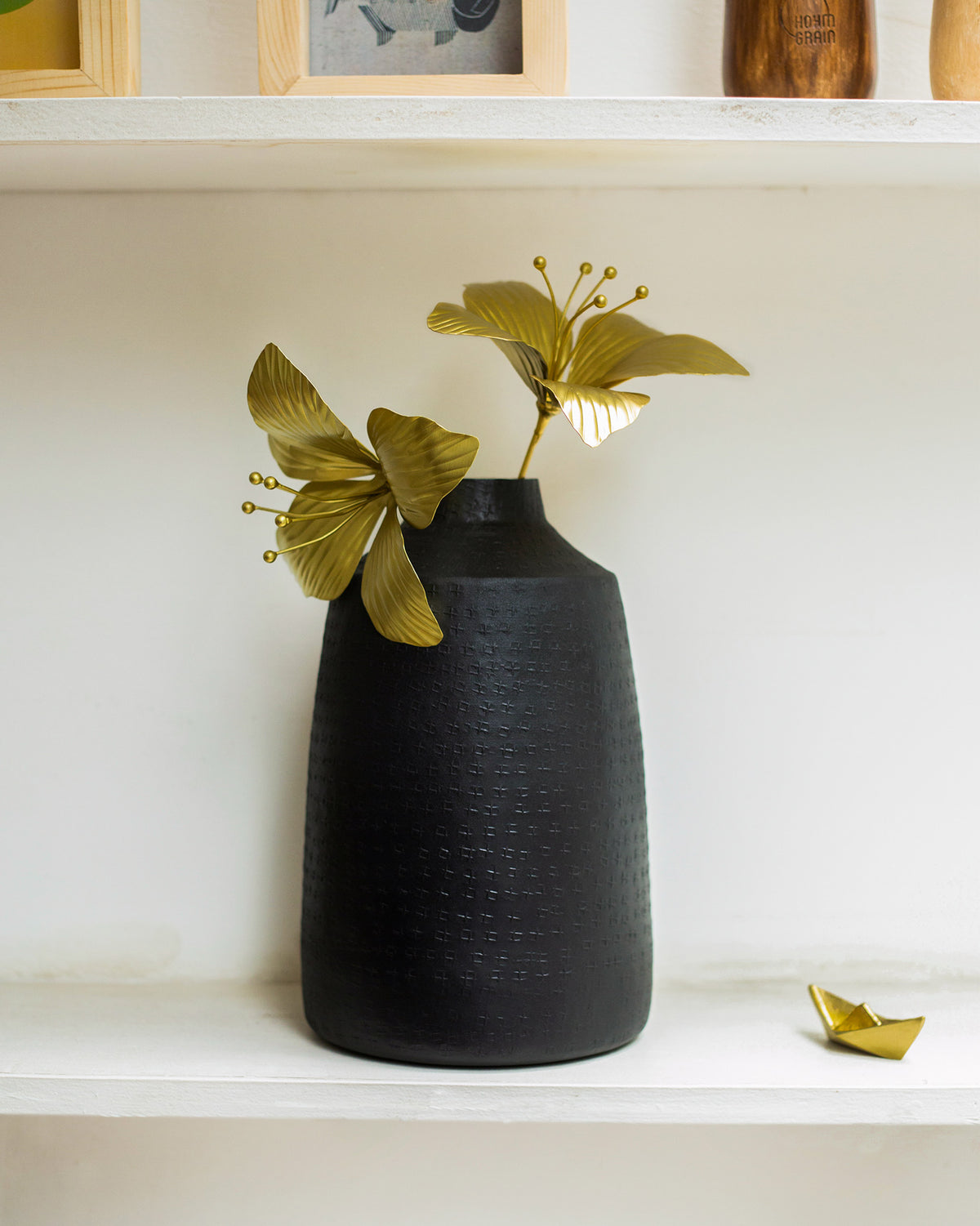 Gold Kachnar home accents in a black vase on a white shelf.
