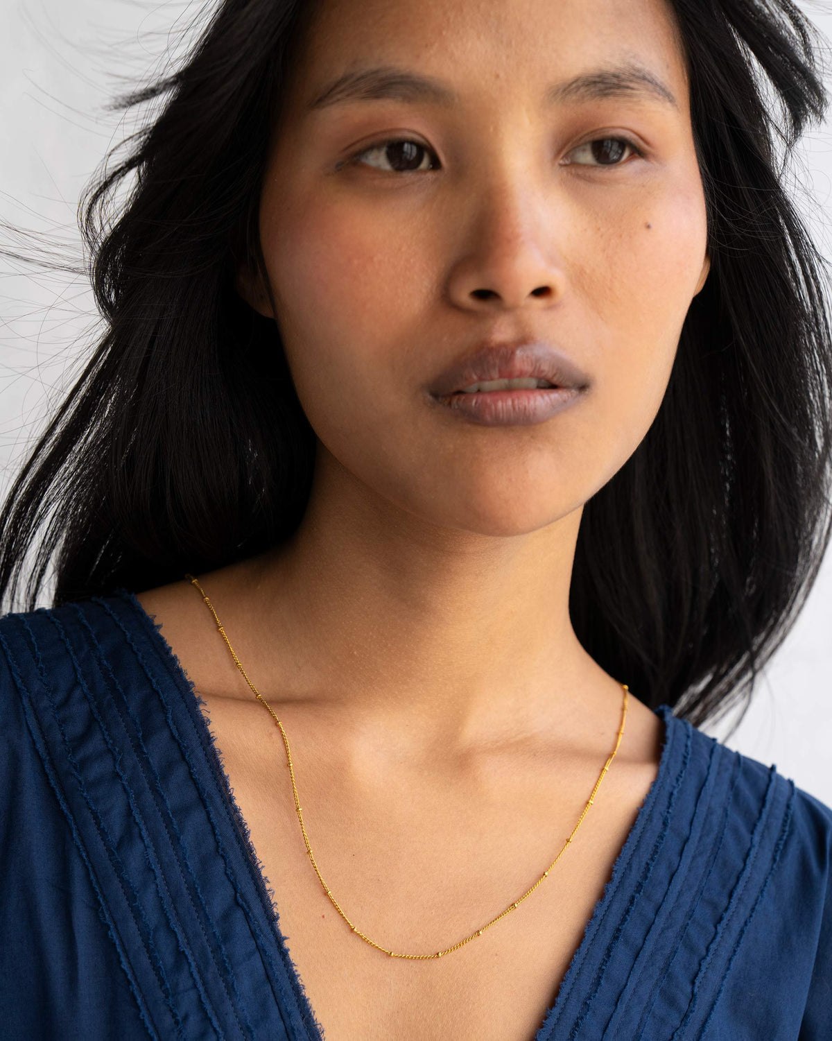 Person wearing small Boondi Chain in gold at the neckline.