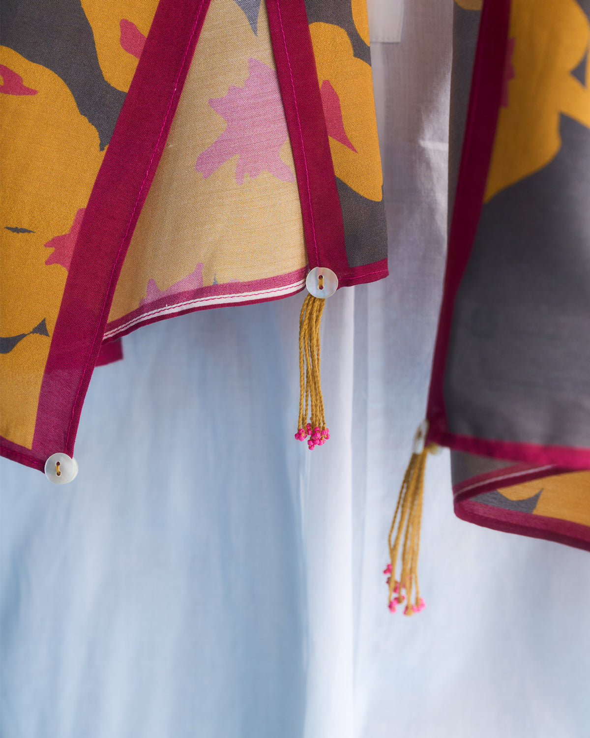 Close-up of a Gudhal scarf edge showing pink trim, a button and a tassel.