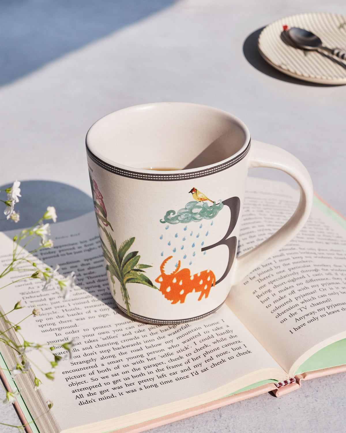 Cream Badal mug with cloud and rain motifs, resting on a book.