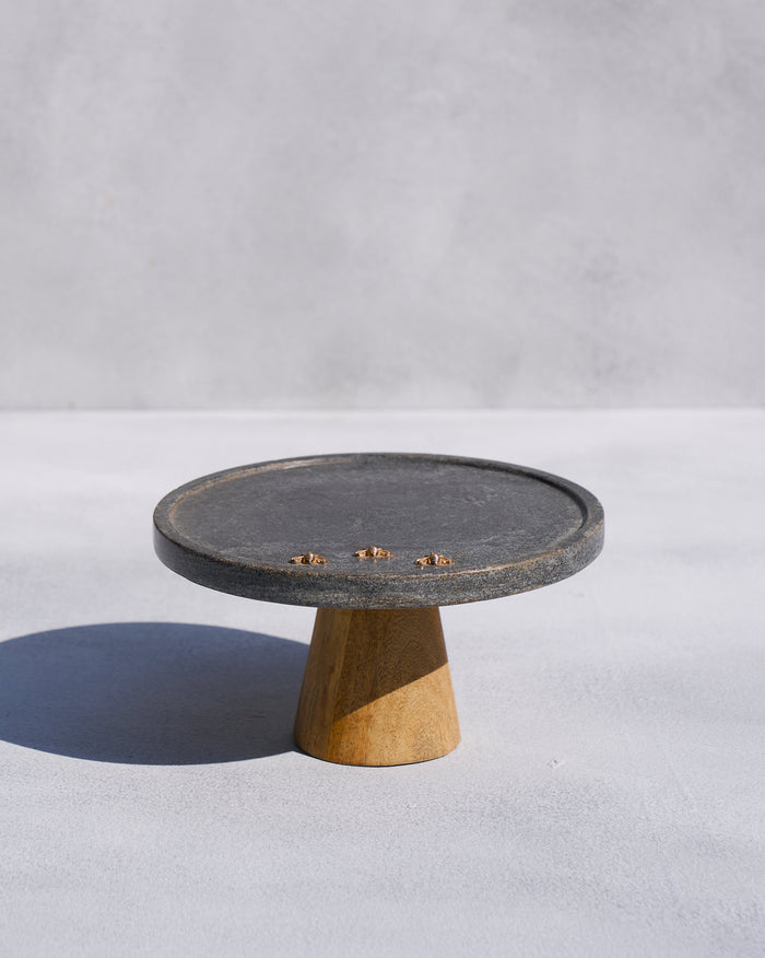 Firefly cake stand with a dark marble top, three gold fireflies, and a wooden pedestal.