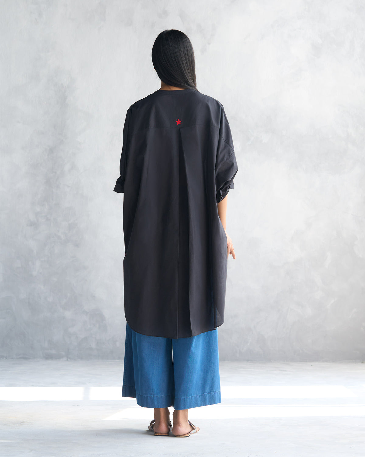 Back of a black Lazy Sunday tunic with a box pleat and red star.