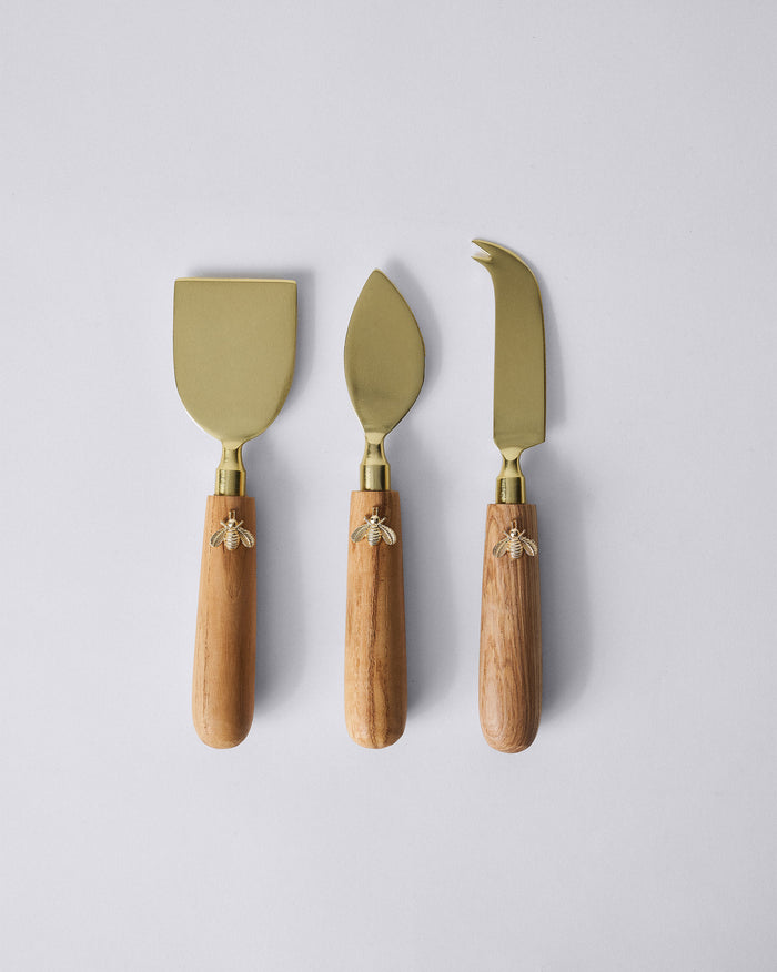 Set of three Garo cheese knives with brass blades, wood handles, and bee charms.