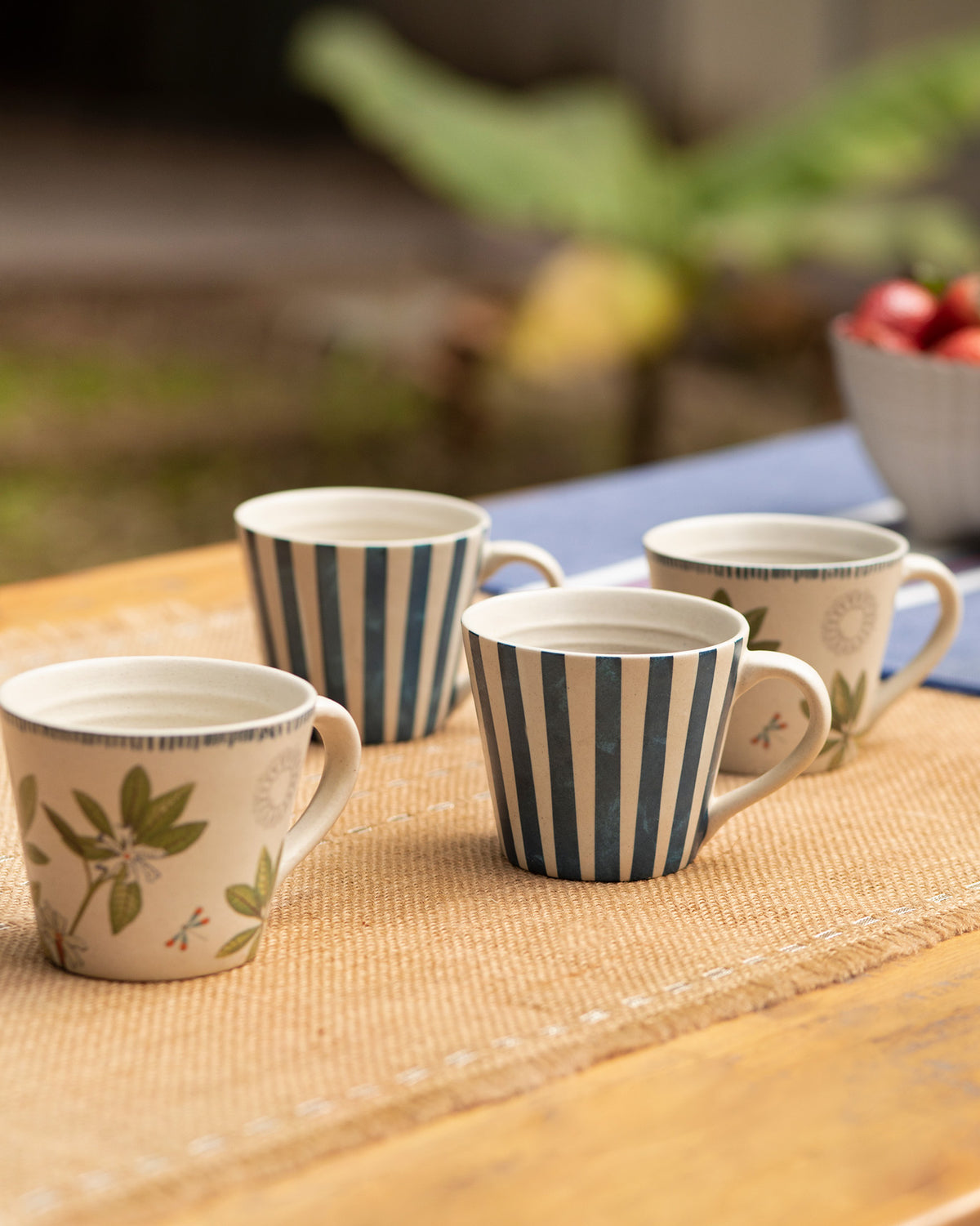 Four Nadi Espresso Mugs, two striped and two with leaf prints, on a wooden table.
