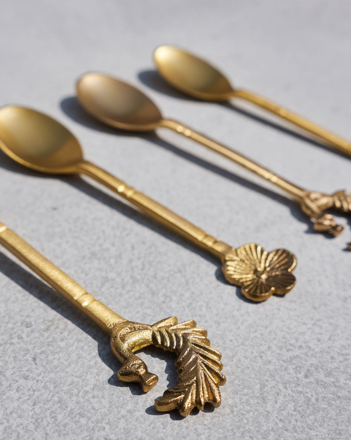 Brass Mizo coffee spoons showing peacock and floral handle tips.