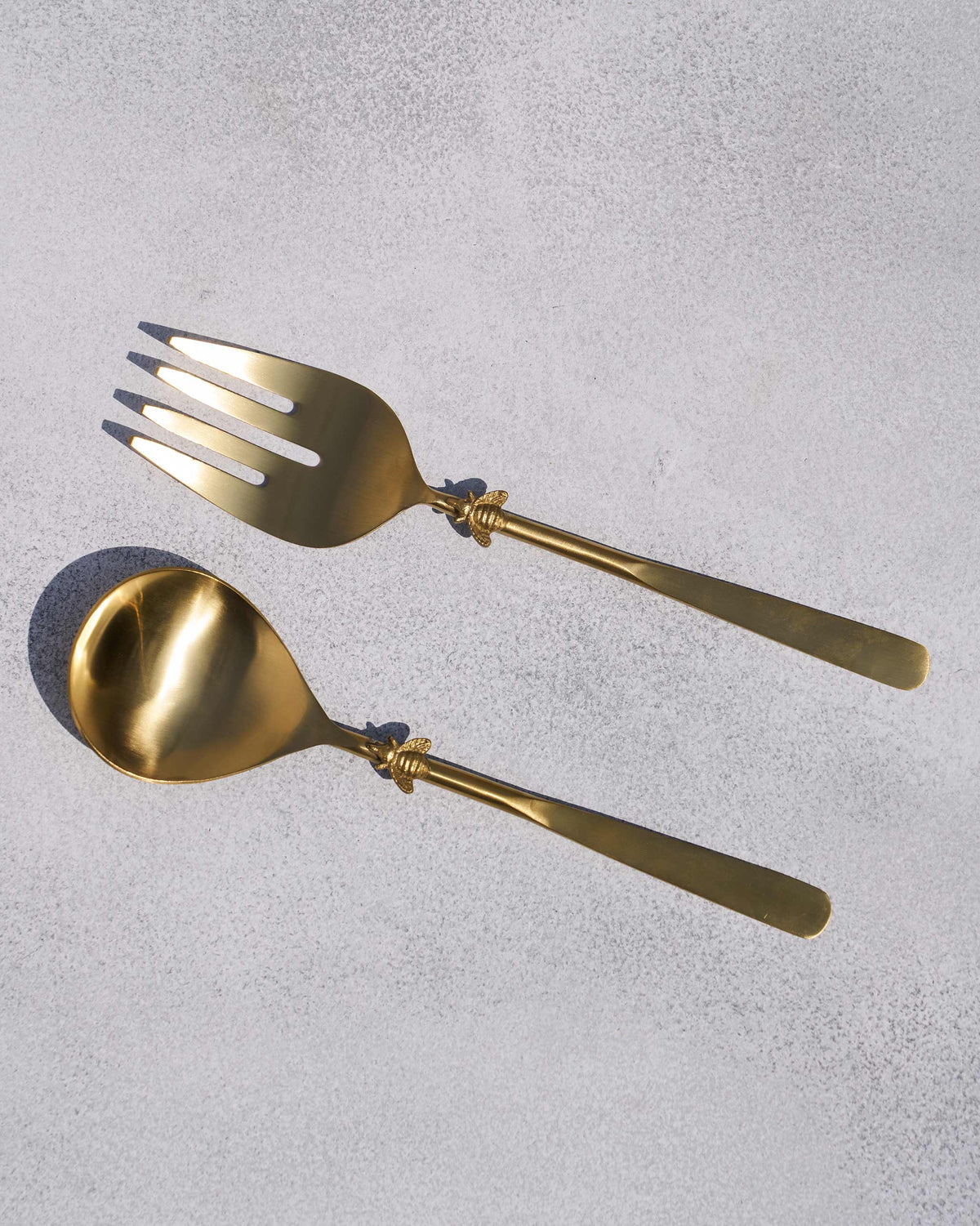 Pair of gold Firefly salad servers with bee motifs on the handles.