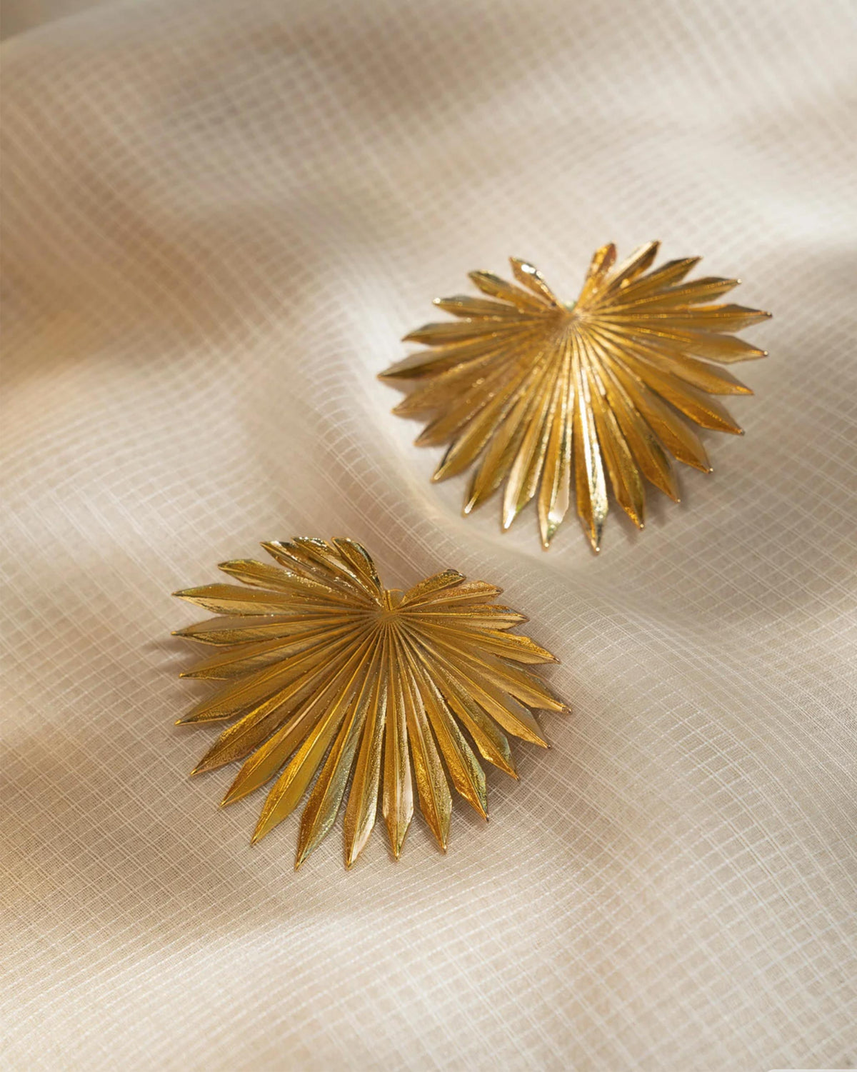Pair of gold palm leaf earrings laid flat.