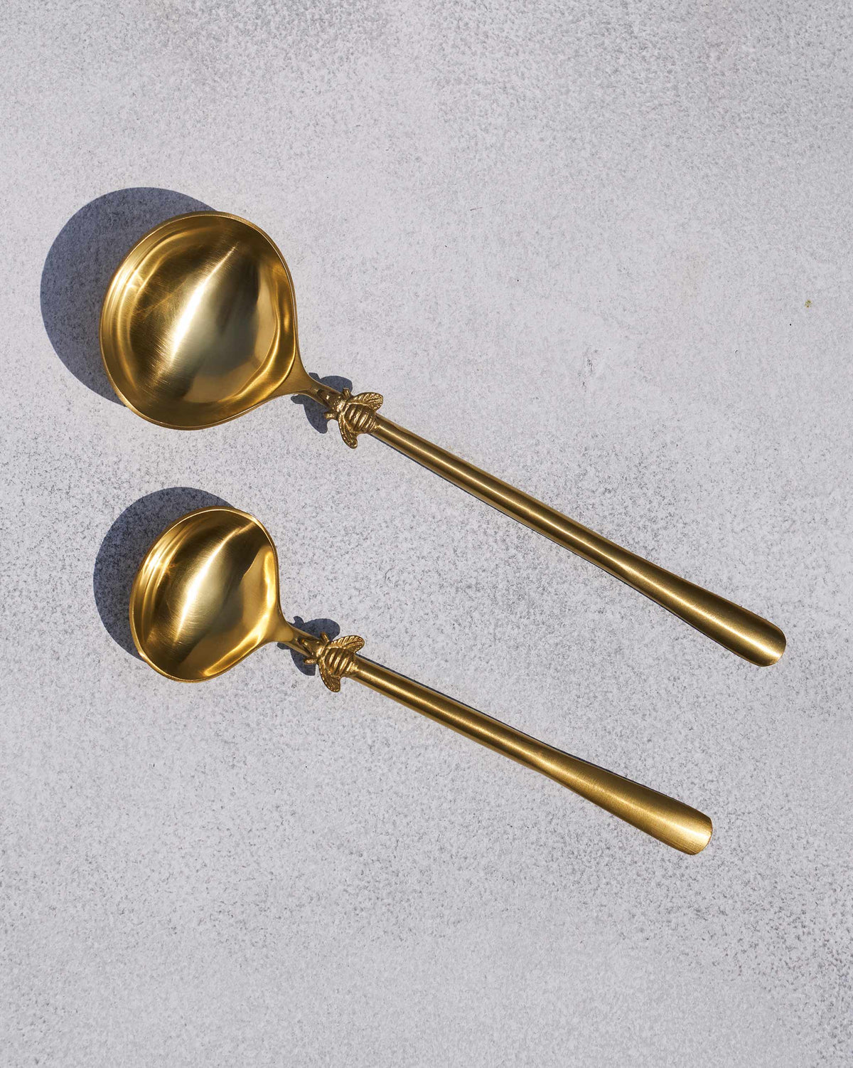 Pair of gold Firefly serving spoons with bee motifs on the handles.
