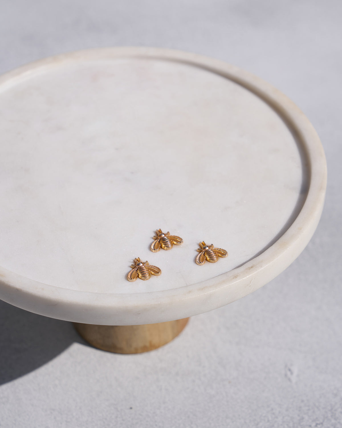 Close-up of the Firefly cake stand showing three gold bee motifs.