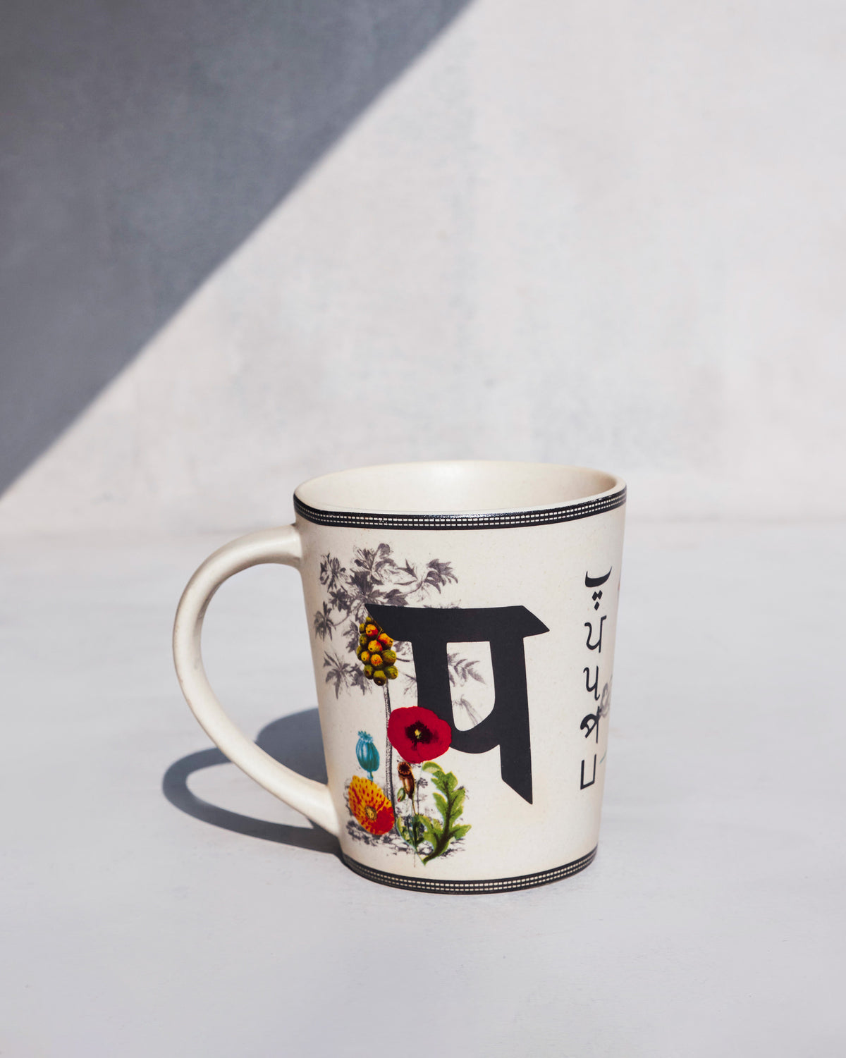 Cream Patang mug with a large Devanagari letter and floral motifs.